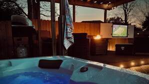 A hot tub with a wooden deck and a TV screen in the background. - Backyard Oasis with Private Pool, SPA and Putting Green only 2 Miles from TAMU! (College Station)