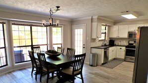 A spacious kitchen with a dining area, featuring a large wooden table, chairs, and a central island with a bowl. - Backyard Oasis with Private Pool, SPA and Putting Green only 2 Miles from TAMU! (College Station)