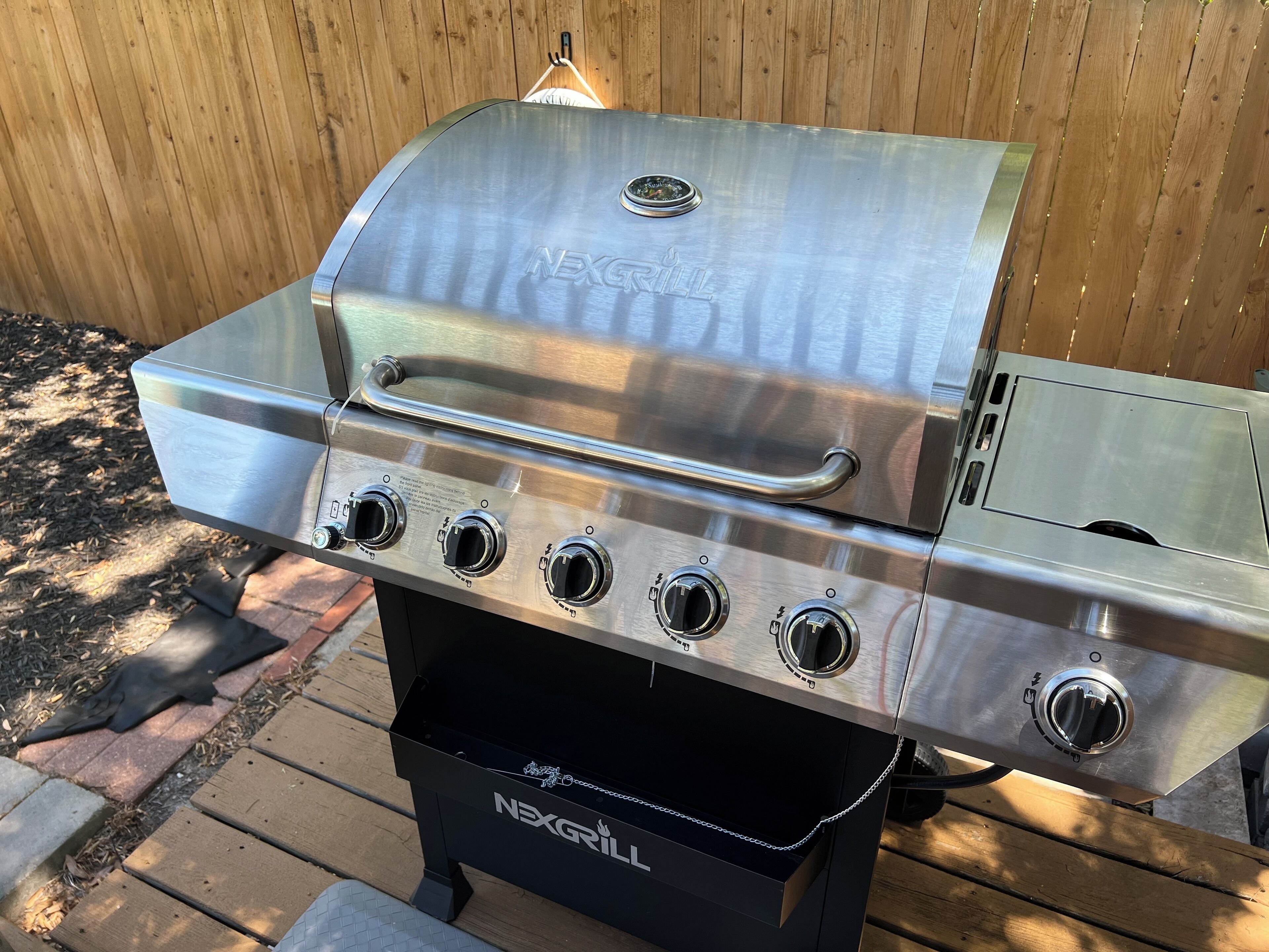A stainless steel NEXGRILL barbecue with four burners and a side shelf, set on a wooden deck.