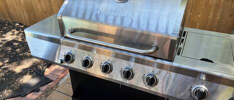 A stainless steel NEXGRILL barbecue with four burners and a side shelf, set on a wooden deck.