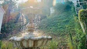 A garden with a central fountain, surrounded by lush greenery and a building with a sign reading "Maison Blanche". - La Maison Blanche B&B with Romantic Outdoor Bath & Panorama View (Chiang Rai)