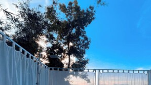 A modern outdoor bathroom with a large bathtub, tiled floor, and a view of trees and sky. - La Maison Blanche B&B with Romantic Outdoor Bath & Panorama View (Chiang Rai)