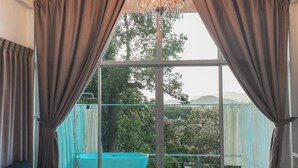 A room with a large window, a dark green sofa, a small table, and a view of a swimming pool and greenery outside. - La Maison Blanche B&B with Romantic Outdoor Bath & Panorama View (Chiang Rai)