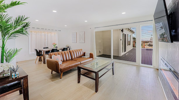 A spacious living room with a brown leather sofa, a glass coffee table, and a dining area with a wooden table and chairs. - 246A- Modern 3B2B w/ Deck & View by Hillsdale Mall (San Mateo)