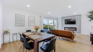 A modern living room with a wooden dining table, black chairs, a sofa, a fireplace, and a TV mounted on the wall. - 246A- Modern 3B2B w/ Deck & View by Hillsdale Mall (San Mateo)