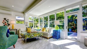 A spacious living room with a large window, a sofa, a chair, and a coffee table. - Vahevala: Your Tranquil Mid-Town Key West Oasis, 3BR Home, Pool & Close to Beaches & Duval Street! (Key West)