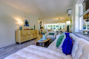 Un salón espacioso con un sofá blanco, un mueble de madera y un comedor con mesa y sillas.