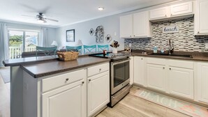 A modern kitchen with white cabinets, a granite countertop, and a backsplash with a beach theme.
