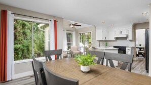 A modern kitchen with white cabinets, a dining area with a wooden table and chairs, and a large sliding glass door leading to a balcony with a view of greenery. - Exceptional Pet Friendly Home, Game Room w/ Pool Table, Large Deck and Seating, 5 Miles to Portland (Portland)
