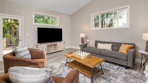 A living room with a flat-screen TV, a grey sofa, a wooden coffee table, and a patterned rug. - Exceptional Pet Friendly Home, Game Room w/ Pool Table, Large Deck and Seating, 5 Miles to Portland (Portland)