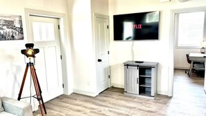 Ein Wohnzimmer mit Holzboden, einer Wandhalterung für den Fernseher, einem Stativ und einem Schrank.