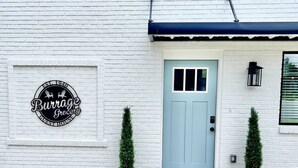 Ein weißes Gebäude mit einer hellblauen Tür, zwei Topfpflanzen und einem Schild mit der Aufschrift 'Burrage Grocery'.