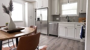 A modern kitchen with white cabinetry, a stainless steel refrigerator, and a dining area with a wooden table and chairs. - Modern Nest - Brand New House w/ modern amenities (Bryan)