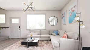 A modern living room with a sectional sofa, a coffee table, a round mirror, and a floor lamp. - Modern Nest - Brand New House w/ modern amenities (Bryan)