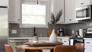 A modern kitchen with white cabinets, a wooden dining table, and brown chairs. - Modern Nest - Brand New House w/ modern amenities (Bryan)