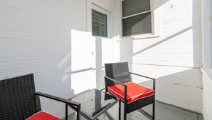 Un balcon avec deux chaises et une table en verre, des murs blancs et deux fenêtres équipées de stores.
