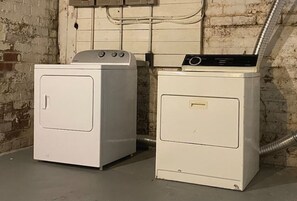 Two white washing machines in a room with a brick wall and exposed pipes.