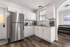 A modern kitchen with white cabinets, a stainless steel refrigerator, a microwave, and a coffee maker.