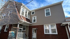 Une maison à deux étages avec un porche à l’avant, un garage et une façade en briques.