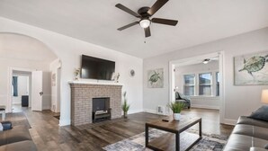 Un salon spacieux doté d’une cheminée, d’un ventilateur de plafond et d’un grand téléviseur fixé au mur.