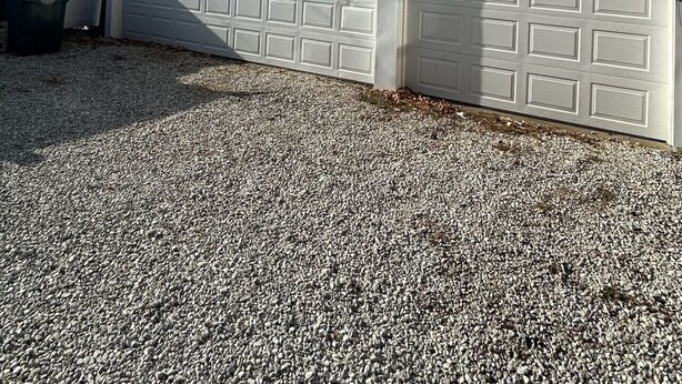 Un garage attenant à une maison, avec une allée en gravier et un ciel bleu dégagé.