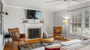 Una sala de estar con chimenea, televisor y un ventanal con persianas.