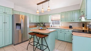 Una cocina con armarios color turquesa, un refrigerador de acero inoxidable, una isla central con taburetes e iluminación colgante.