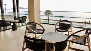 Un balcone con sedie in vimini e un tavolo, con vista su una spiaggia con persone e una palma.