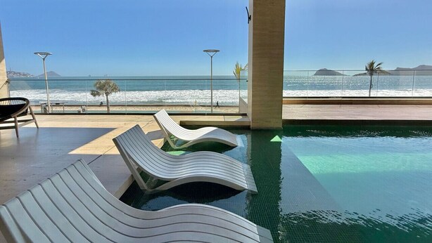 Zona piscina con lettini e vista sulla spiaggia e sull'oceano.