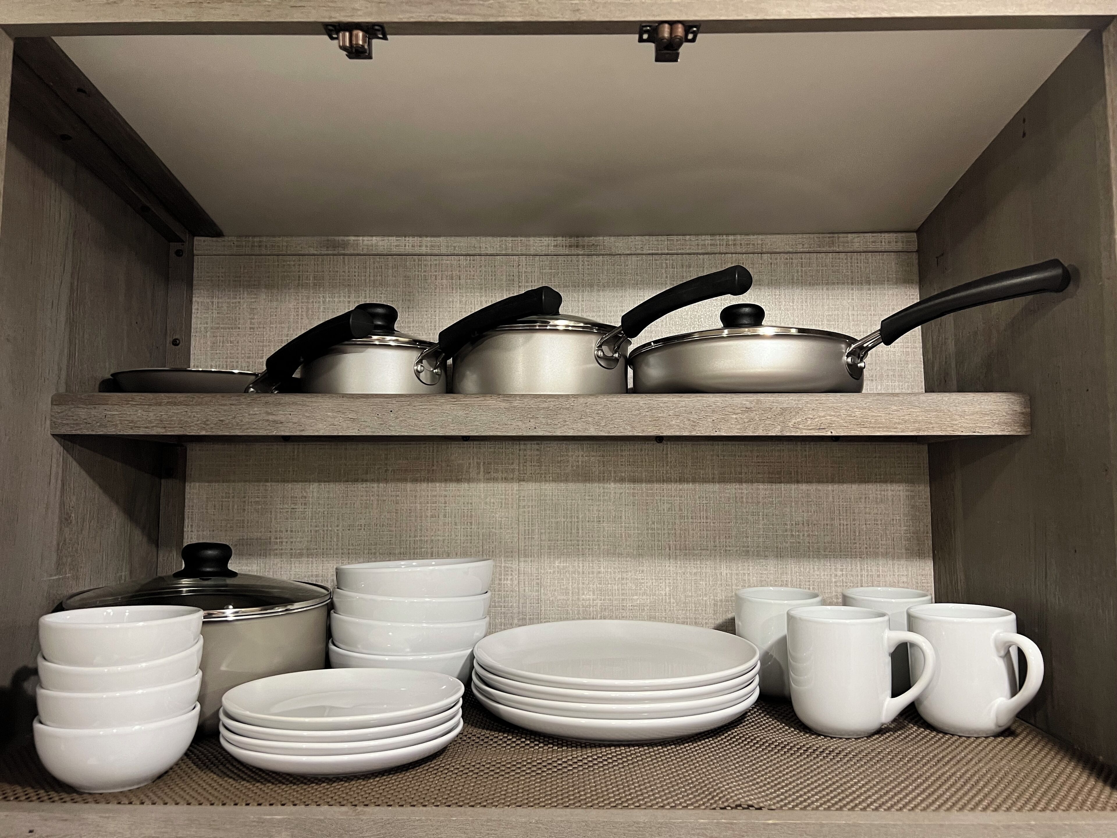 Une étagère de cuisine avec des casseroles, des poêles, des assiettes et des tasses.