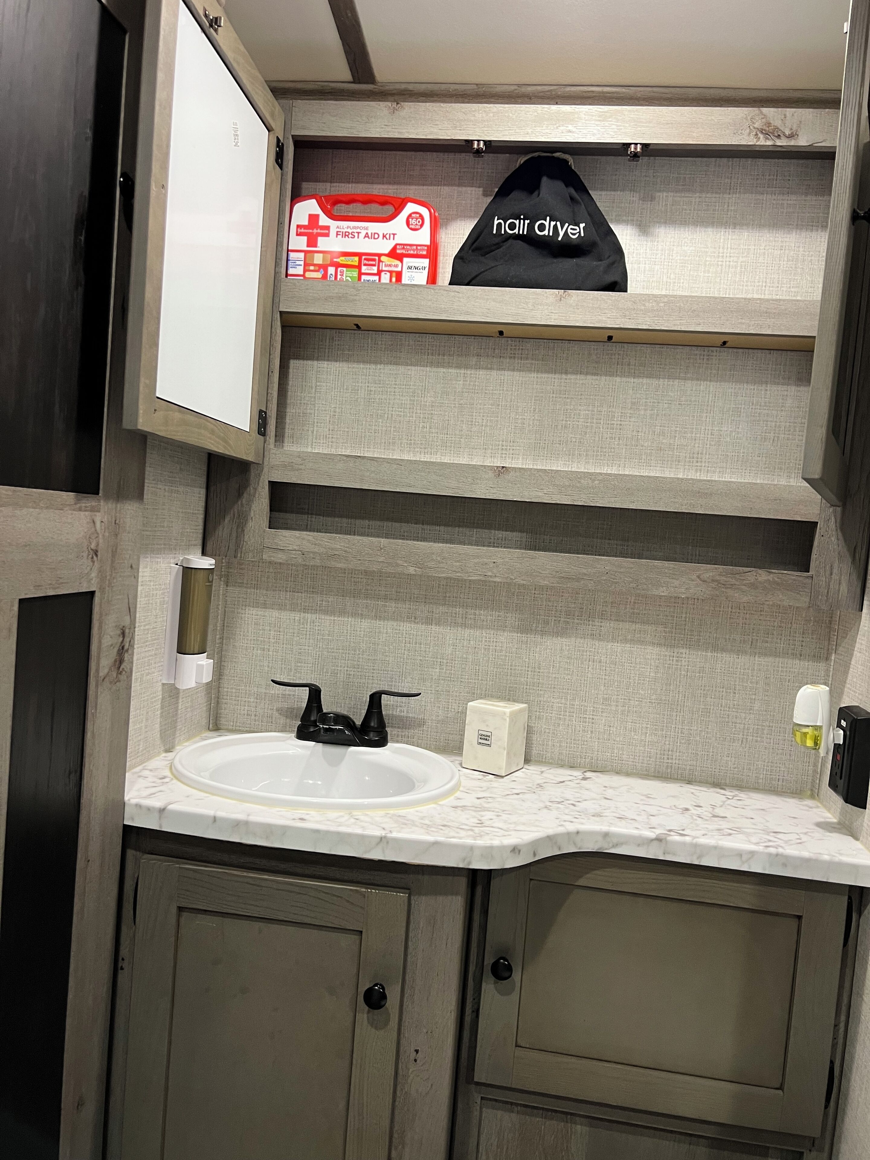 Un baño con un lavabo blanco, un secador de pelo y un botiquín en un estante.