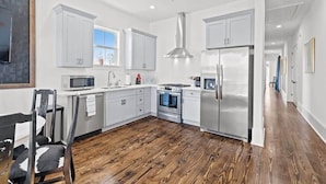 A modern kitchen with white cabinets, stainless steel appliances, and a wooden floor. - Pristine 4BD w Pool | Driveway Parking | Balcony (New Orleans)