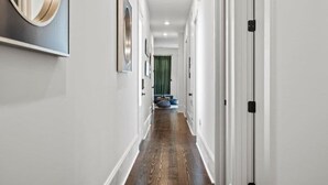 Een gang met witte muren, kunstwerken in lijsten en een houten vloer die leidt naar een kamer met een groen gordijn.