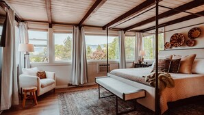 Une chambre à coucher avec un lit à baldaquin, un banc, une chaise et une vue sur l’extérieur.