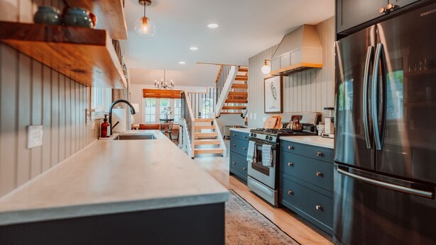 Une cuisine moderne dotée d’un îlot central, d’appareils électroménagers en acier inoxydable et d’un escalier en bois menant à un autre niveau.