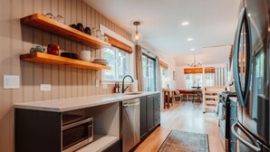 Une cuisine moderne avec des étagères en bois, un four encastré et un coin repas comprenant une table et des chaises.