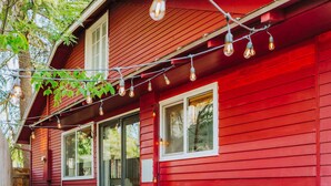 Une maison rouge dotée d’un patio aménagé avec des meubles en bois et des guirlandes lumineuses.