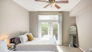 A hotel room with two beds, a ceiling fan, a large window with a view, and a mirror. - Charming 1,100 sq. ft. apt (Plano)