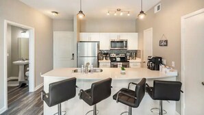 A modern kitchen with a central island, stainless steel appliances, and bar stools. - Charming 1,100 sq. ft. apt (Plano)