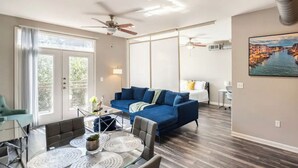 A modern living room with a blue sofa, a dining table with chairs, and a ceiling fan. - Charming 1,100 sq. ft. apt (Plano)