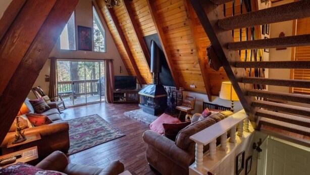Una sala de estar estilo loft acogedora con chimenea, vigas de madera y un ventanal con vistas a una terraza.