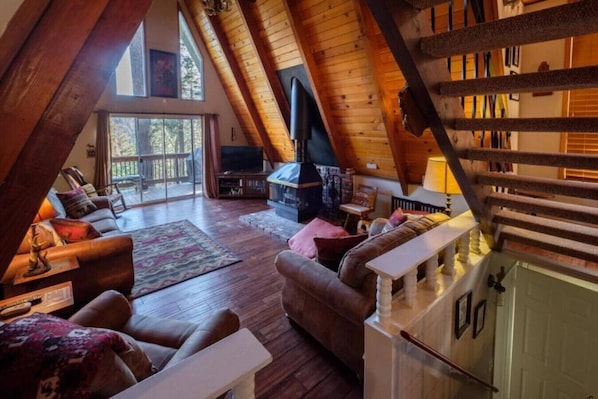 Una sala de estar estilo loft acogedora con chimenea, vigas de madera y un ventanal con vistas a una terraza.