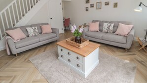 A living room with two grey sofas, a wooden coffee table, and a herringbone-patterned floor. - The Miners Cottage (Berwick-upon-Tweed)