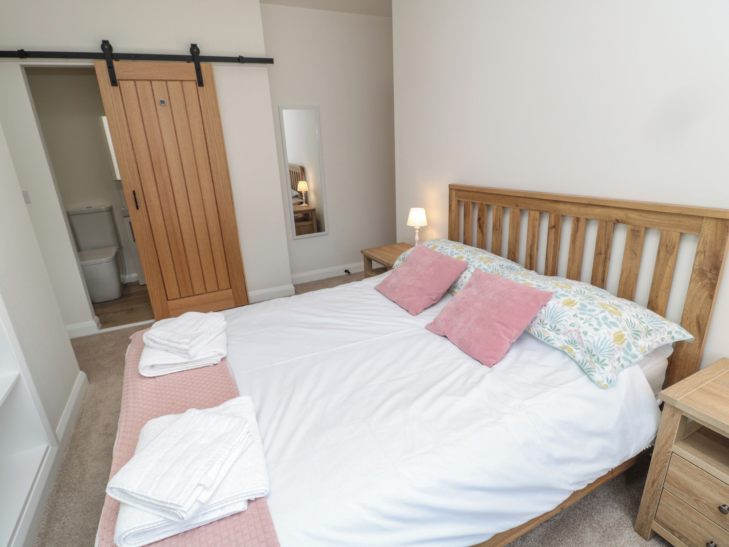A bedroom with a bed, a wooden headboard, a nightstand, a bedside table, a mirror, and a sliding door closet.