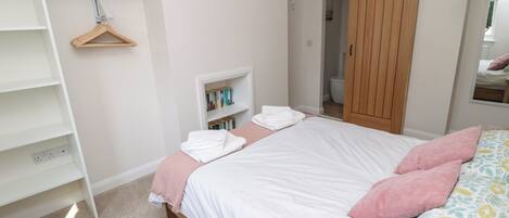 A bedroom with a bed, a wardrobe, a shelf with books, and a hanging rack.