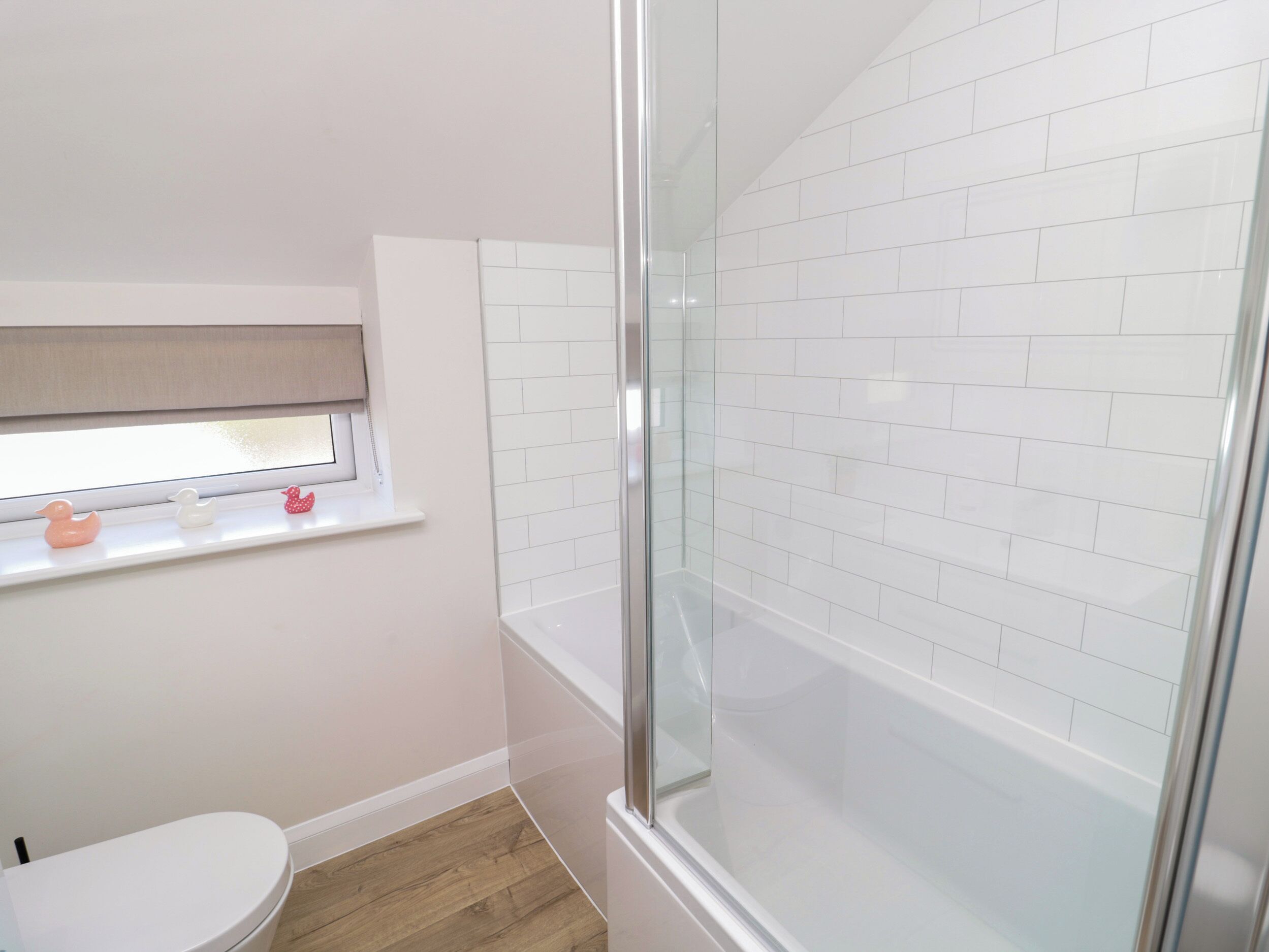 A bathroom with a toilet, a window with a shelf, and a shower area with white tiles.
