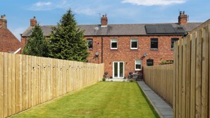 A residential property with a paved pathway leading to a brick house with a green lawn and a wooden fence. - The Miners Cottage (Berwick-upon-Tweed)
