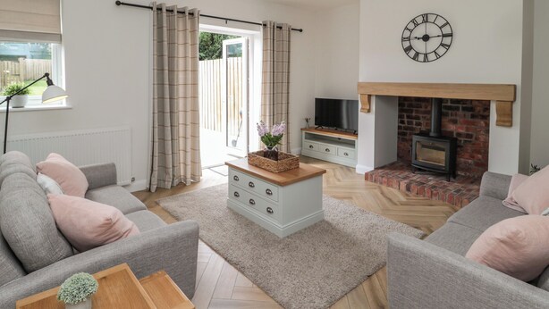 A modern living room with grey sofas, a wooden coffee table, a fireplace, and a TV on a stand. - The Miners Cottage (Berwick-upon-Tweed)