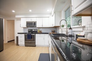 A modern kitchen with white cabinets, stainless steel appliances, and a black countertop. - Lakeside home on Horseshoe Lake: kayaks, paddle boards, fire pit, games, fishing (Port Orchard)