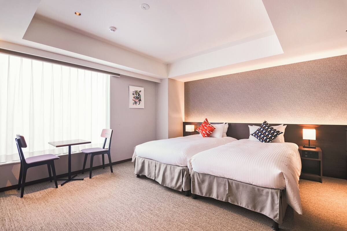 A hotel room with two beds, a desk, and chairs.